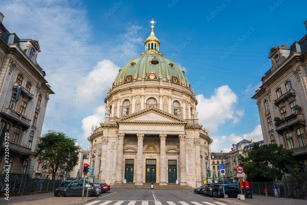 Copenhagen's Frederik's Church, The Marble Church, has a rococo style and a green copper dome with a gold orb and cross. Its grand front showcases Corinthian columns under a striking sky.