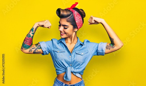 Strong Latino woman with tattoos and red bandana dressed as US WW2 industry icon Rosie the Riveter, flexing her muscles
