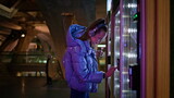 Woman buying snacks vending machine at subway late evening. Girl make purchase.