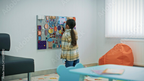 Little girl draws on entertainment board with toys in the waiting area in modern hospital. Child waits for appointment with family doctor in clinic. Concept of children medicine and healthcare. photo