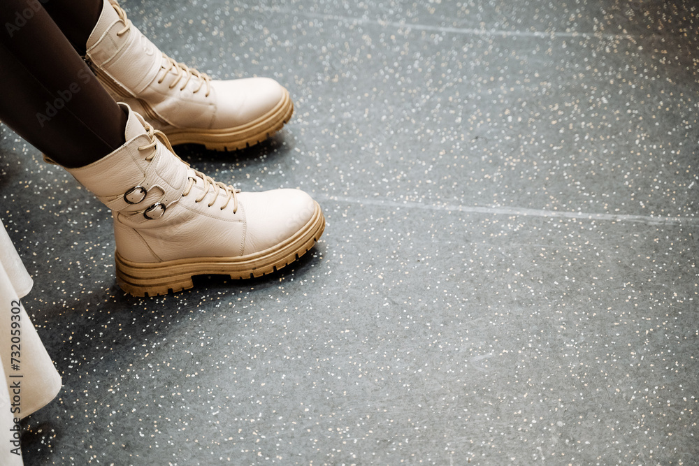 Person Wearing Stylish White Boots Sitting on Grey Floor with White Speckles Person Wearing Stylish White Boots Sitting on Grey Floor with White Speckles