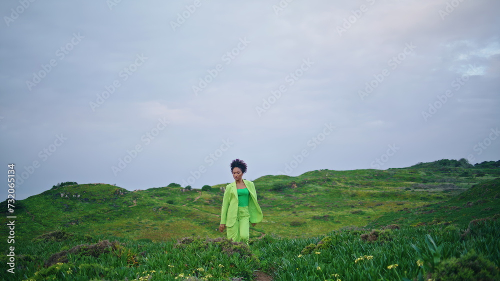 Fototapeta premium Stylish girl dancer performing modern style dance on green field under gray sky.