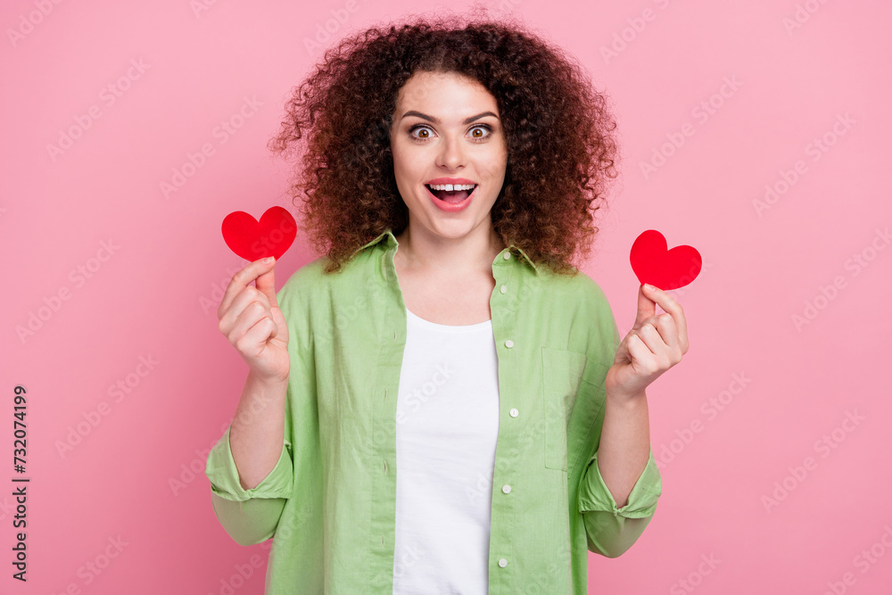 Photo portrait of attractive young woman hold excited two heart postcards wear trendy green clothes isolated on pink color background Photo portrait of attractive young woman hold excited two heart postcards wear trendy green clothes isolated on pink color background