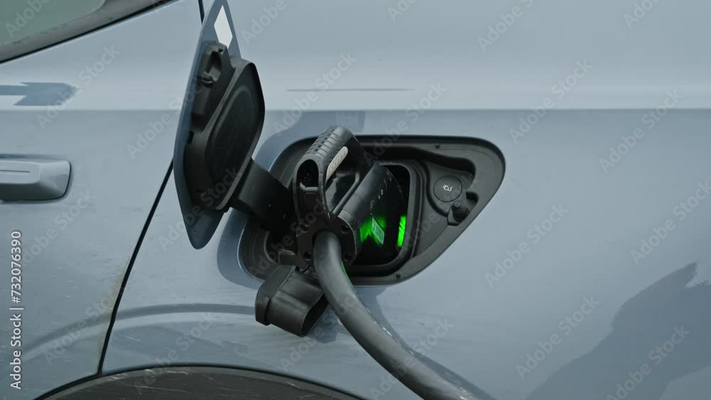 Electric Car with Plug In Charger Reacharging Battery on Outdoor Parking Lot 