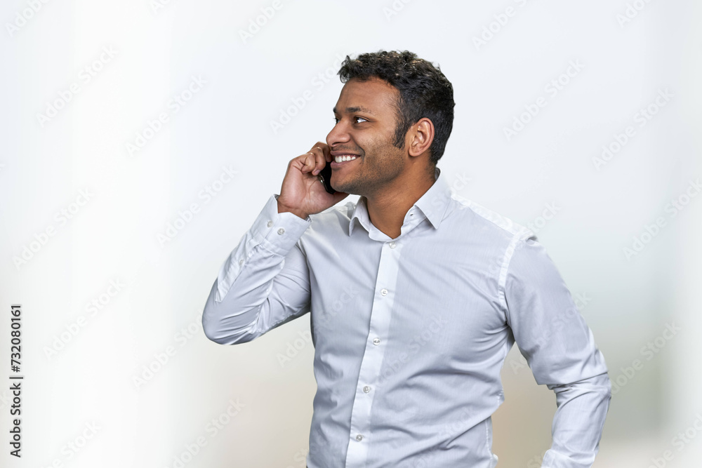 Side view of smiling young businessman talking on cell phone on blurred background. Handsome man in white shirt talks on mobile phone with a smile. Side view of smiling young businessman talking on cell phone on blurred background. Handsome man in white shirt talks on mobile phone with a smile.
