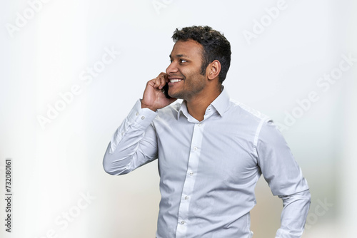 Side view of smiling young businessman talking on cell phone on blurred background. Handsome man in white shirt talks on mobile phone with a smile.