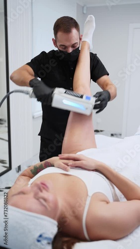 Therapist performs endospheres therapy on clients leg, targeting cellulite reduction, lymphatic drainage in spa setting. Patient relaxes while receiving non-invasive body contouring treatment. photo