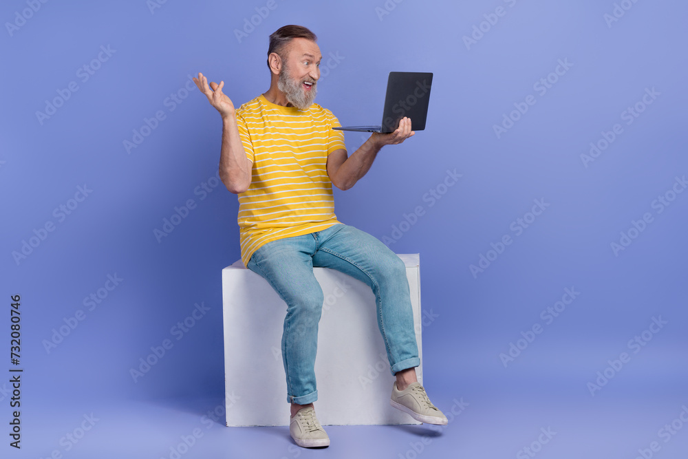 Full length portrait of handsome grandfather sit podium speak video call laptop empty space isolated on purple color background Full length portrait of handsome grandfather sit podium speak video call laptop empty space isolated on purple color background