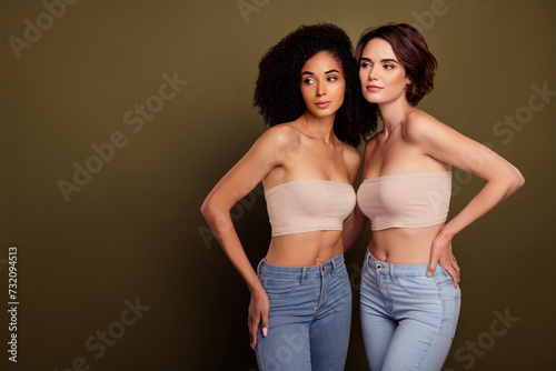 Photo of two beautiful women lgbt pride wearing crop tops combinated with jeans isolated on khaki color background photo