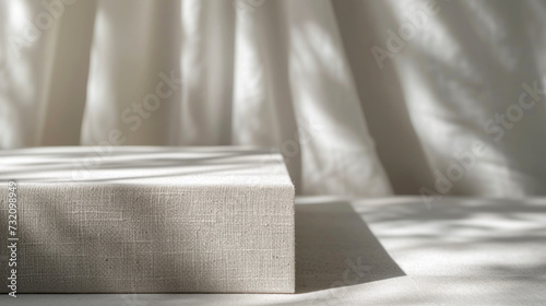 Abstract light interior. White fabric box on the table with sunlight and shadow on the wall. Product mockup close up, natural gray materials. Interior in minimalist style. Close-up textures.
