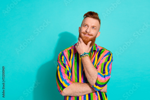 Portrait of young thoughtful red haired successful business man touch chin his long beard look novelty isolated on blue color background