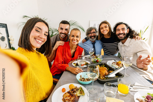 Group of multi-generational family enjoying dinner party taking selfie portrait sitting together at living room table.