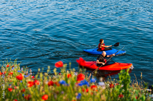 Two kayakers paddle the Tennessee River beneath the Walnut Street Bridge in Chattanooga. Blue and red flowers in the foreground match the colors of the kayaks.
