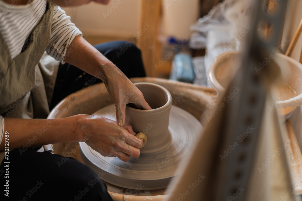An artist shapes a clay pot with precise movements on a spinning pottery wheel.