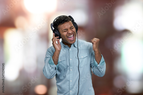 Ecstatic young man enjoying listening to music with headphones. Abstract bokeh background.