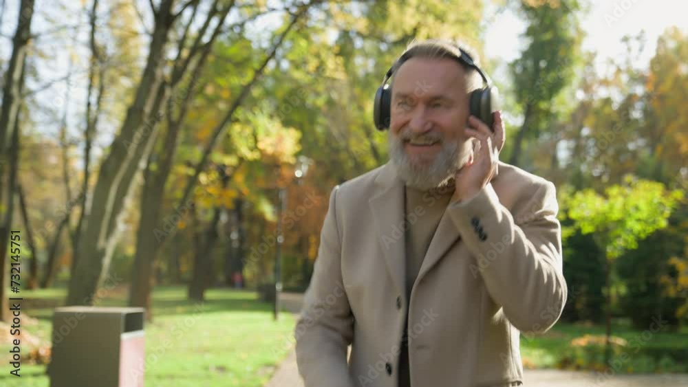 Mature senior bearded man in elegant outfit dancing at autumn park funny positive 70s aged gentleman businessman happy male relaxing dancing in city outdoors listening music headphones enjoying song
