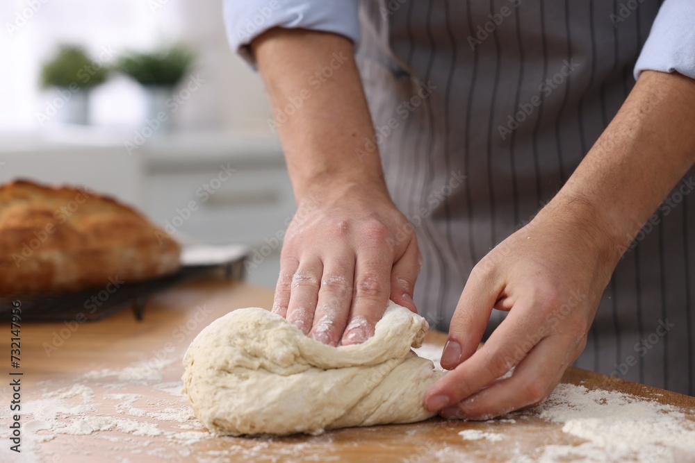 Making bread. Man kneading dough at wooden table in kitchen, closeup