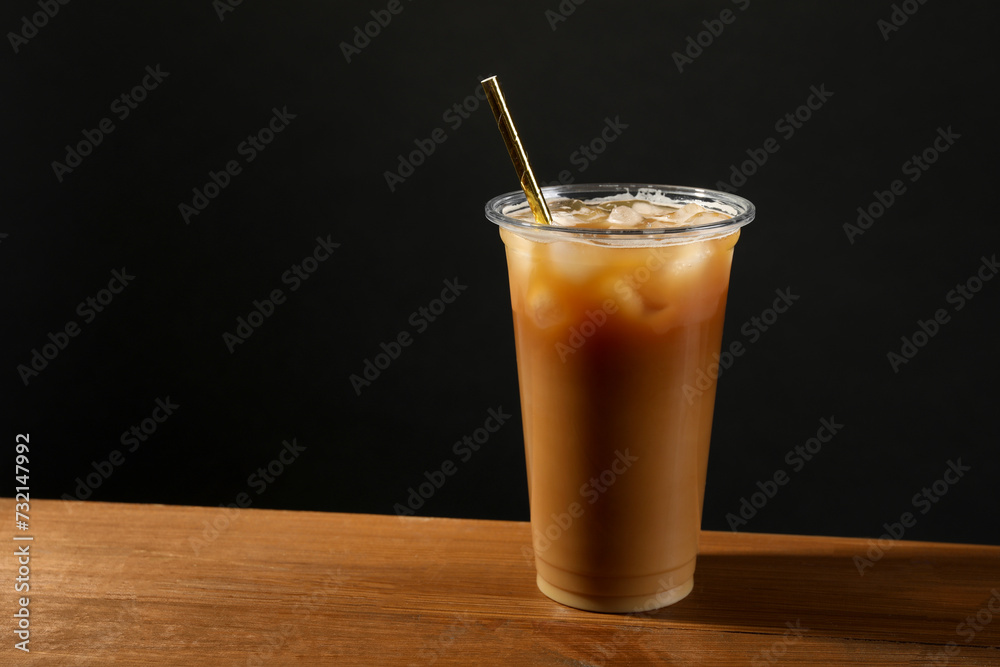 Refreshing iced coffee with milk in takeaway cup on wooden table against black background, space for text