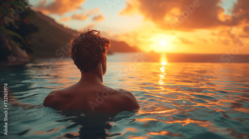 Luxury swimming pool in a tropical resort, relaxing holidays in Seychelles islands. La Digue, Young man during sunset by swim pool, men watching the sunset in an infinity pool photo