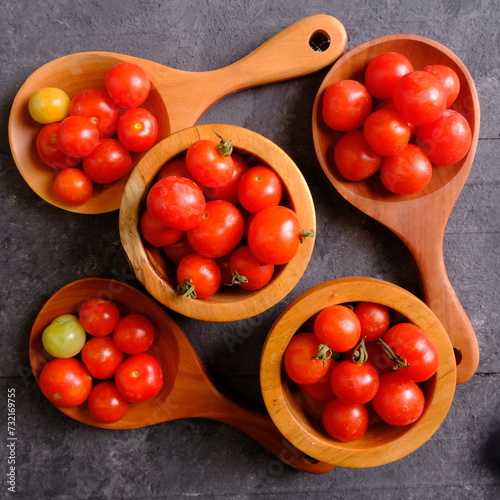 Fresh cherry tomatoes in wooden spoon on black wooden rustic table. Contains vitamins C, A, lycopene. Solanum lycopersicum var. cerasiforme. Cherry tomato. Tomat Ceri. 
 photo