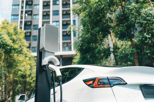 Fototapeta Naklejka Na Ścianę i Meble -  EV electric car charging in green sustainable city outdoor garden in summer. Urban sustainability lifestyle by green clean rechargeable energy of electric BEV vehicle innards