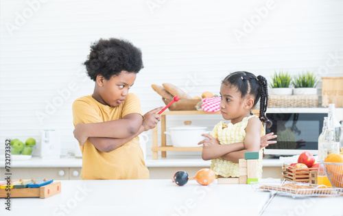 Angry african brother and little sister madly looking at each other with arms crossed gesture while playing toys together at home kitchen. Siblings children conflict concept
