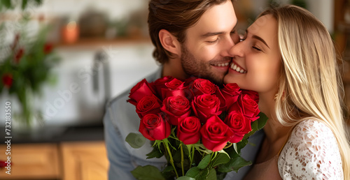 Happy couple, red roses and kiss for surprise, anniversary or valentines day in kitchen at home. Face of young man and woman smile with flowers for romantic gift, love or care in celebration