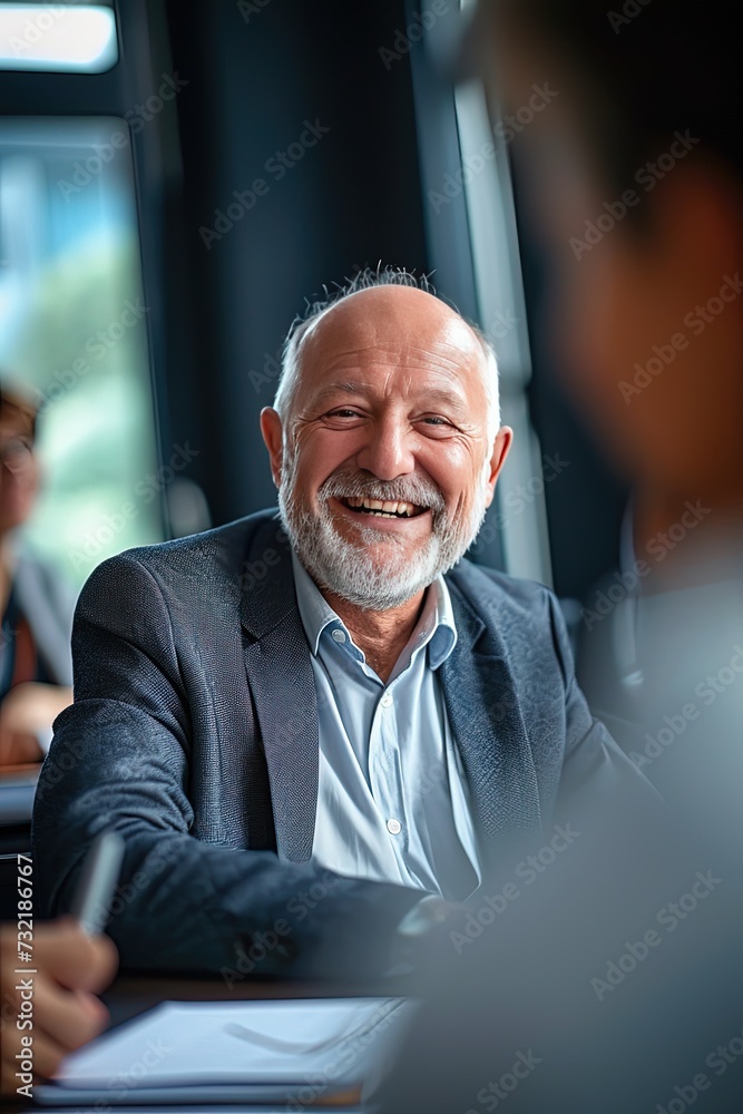 Senior businessman smiling during a meeting in the office. The senior executive's smile reflects his satisfaction with the meeting's progress. Senior businessman smiling during a meeting in the office. The senior executive's smile reflects his satisfaction with the meeting's progress.