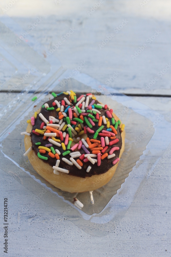 Chocolate topping donuts and colorful sprinkles in mica plastic on a wooden table