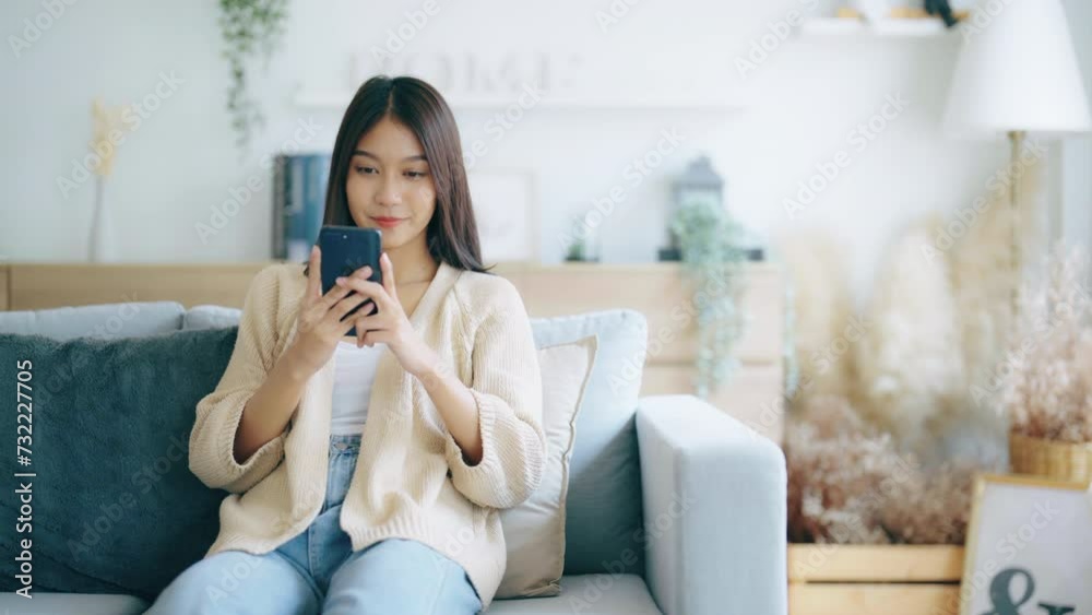 Happy young asian woman relax on comfortable couch at home texting messaging on smartphone, smiling girl use cellphone chatting, browse wireless internet on gadget, shopping online from home Happy young asian woman relax on comfortable couch at home texting messaging on smartphone, smiling girl use cellphone chatting, browse wireless internet on gadget, shopping online from home