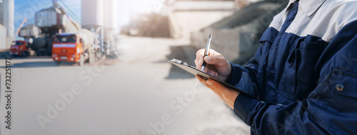 Concept banner automated logistics online internet. Dump truck driver man in uniform with tablet computer controls loading of cement to mixer on factory
