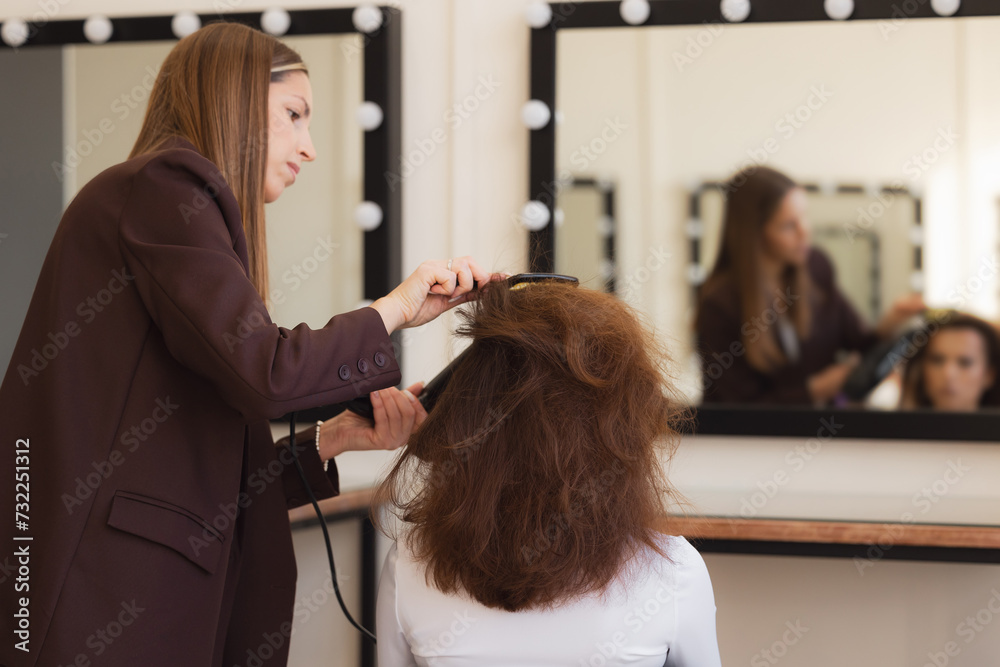 Woman hairdresser making hairstyle to brunette girl in beauty salon Woman hairdresser making hairstyle to brunette girl in beauty salon