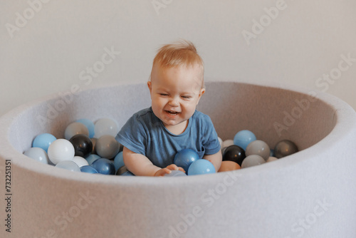 Happy little boy smile and play in dry pool with colorful balls in living room. Concept lifestyle childhood moment photo