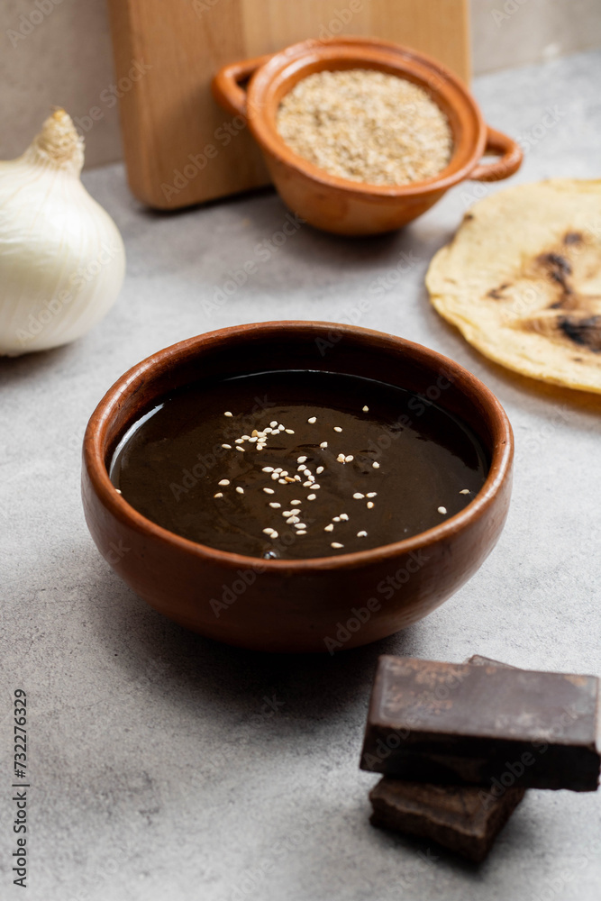 Talavera and clay dish filled with black mole, accompanied by tortillas and sesame seeds, on a cement background in Oaxaca Talavera and clay dish filled with black mole, accompanied by tortillas and sesame seeds, on a cement background in Oaxaca