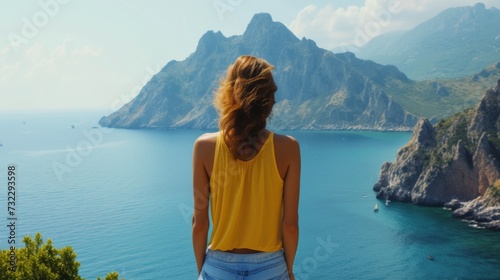A young woman stands with her back and admires the view of the sea and mountains. A traveler traveling on vacation in the most beautiful place in the world. Summer vacation © Vladimir