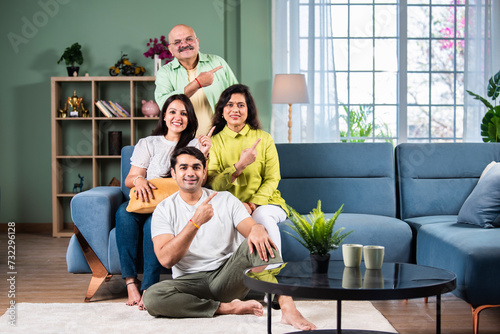 Happy Indian family of four pointing finger for promotion with copyspace.