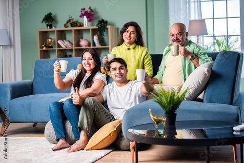 Cheerful Indian family enjoying tea or coffee together, looking at the camera