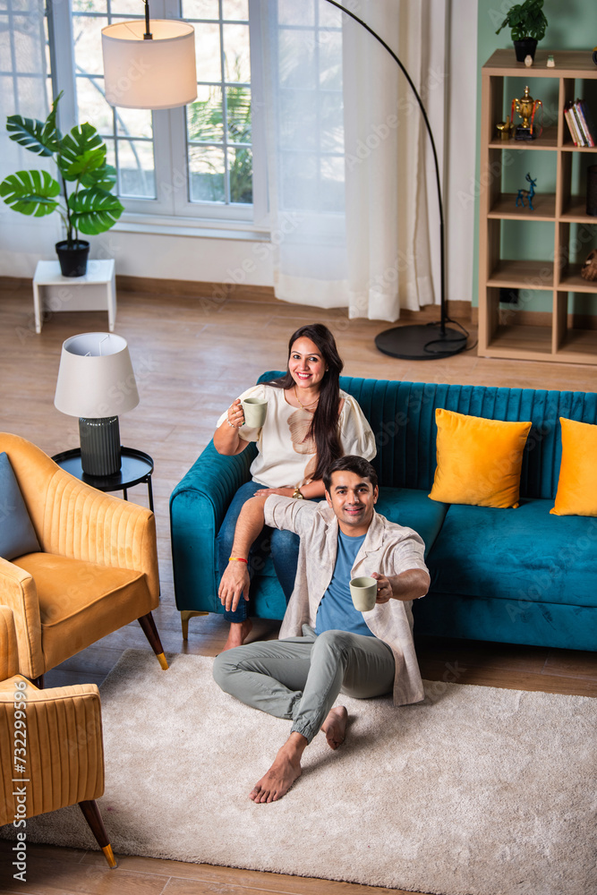 Obraz premium Cheerful young beautiful Indian couple having coffee together on sofa at home..