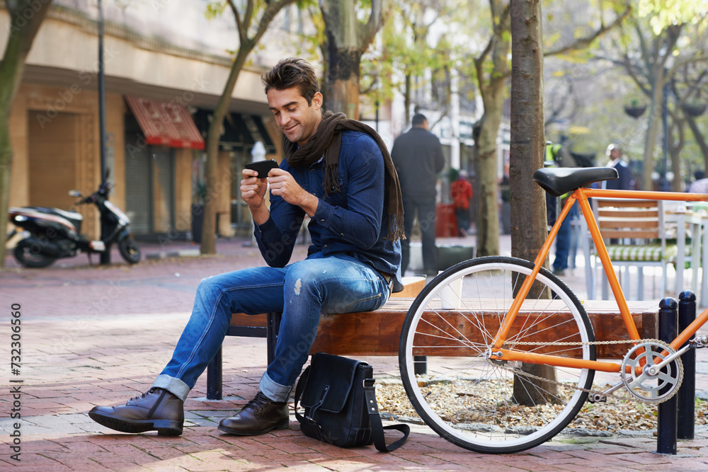 Phone, bike and business man in city, sitting on bench for break with social media browsing or app. Smile, contact and bicycle with confident young employee typing text message outdoor in urban town Phone, bike and business man in city, sitting on bench for break with social media browsing or app. Smile, contact and bicycle with confident young employee typing text message outdoor in urban town