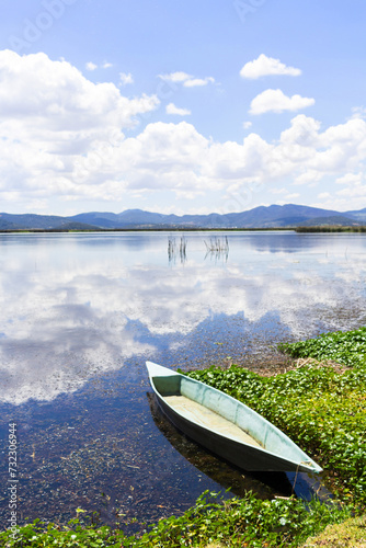 green boat on the shore of lagoon reflecting sky and mountains. beautiful landscape in mexico © cesar