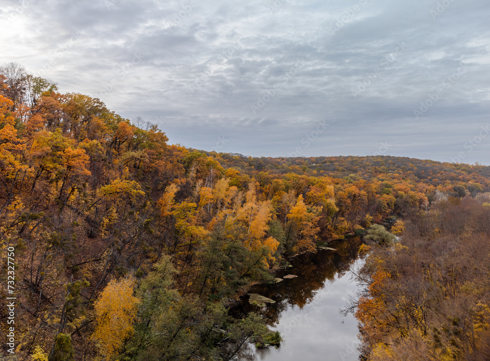 Autumn panorama, aerial river and yellow trees forest landscape with grey cloudy sky. Flying above riverside in Ukraine
