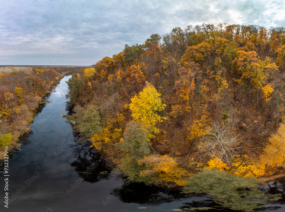 Aerial wide panorama of autumn river with blue mirror water, yellow forest landscape and cloudy sky. Wild riverside in Ukraine