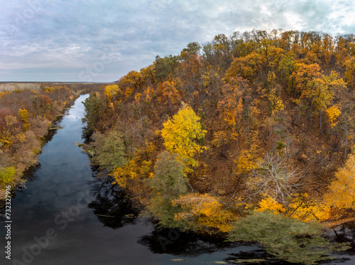 Aerial wide panorama of autumn river with blue mirror water, yellow forest landscape and cloudy sky. Wild riverside in Ukraine