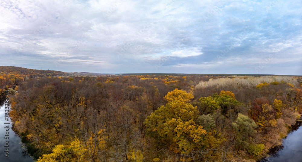 Aerial wide panorama of yellow autumn riverside landscape and cloudy sky. Wild autumnal river valley nature in Ukraine