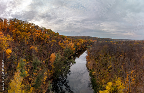 Aerial panorama autumn river with cloudy sky reflection on water surface. Wild colorful autumnal riverside nature in Ukraine