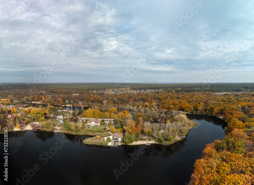 Aerial panorama of autumn river with golden trees forest. Flying above vibrant autumnal village in Ukraine