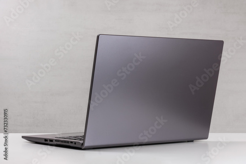 open silver laptop on a white table against a gray wall rear view with a copy space
