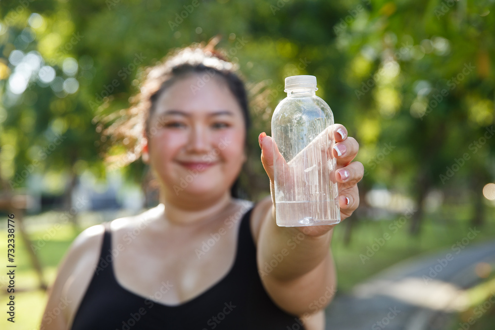 Close up water bottle, women overweight in sportswear drinking water in bottle after exercise in garden, relax and exercise concept. fat female jogging outside. Close up water bottle, women overweight in sportswear drinking water in bottle after exercise in garden, relax and exercise concept. fat female jogging outside.