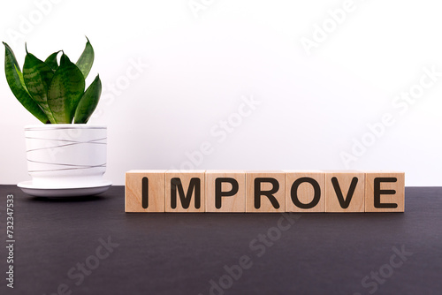 Improve word concept on wooden blocks on a black table with a green flower on a white background