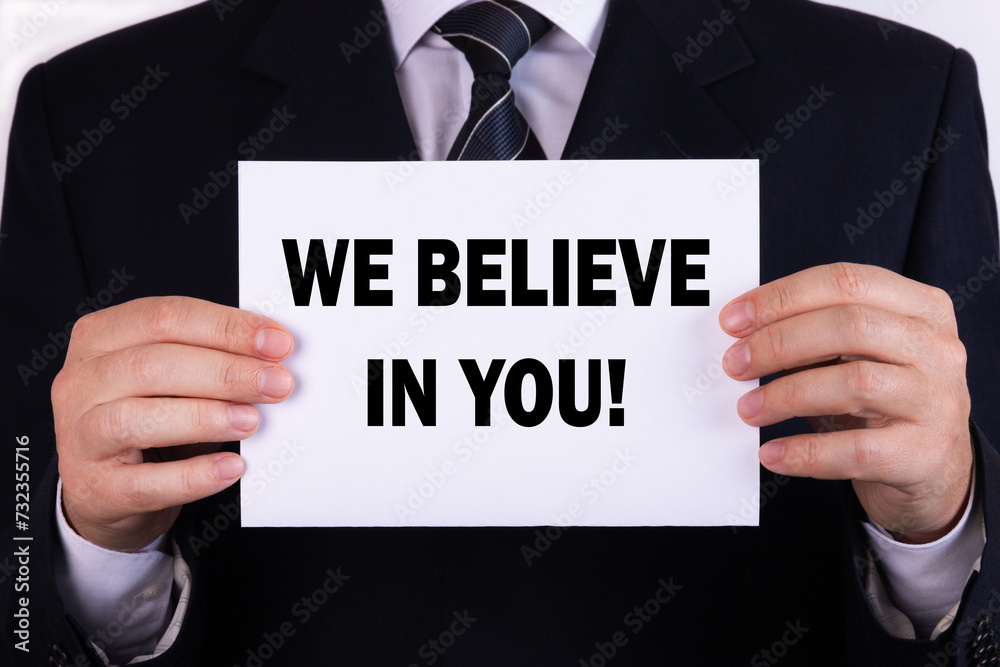 Businessman holding a card with text we believe in you Businessman holding a card with text we believe in you